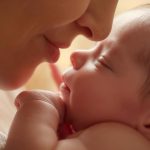 Mutter gibt ihrem schlafenden Neugeborenen einen zärtlichen Kuss auf die Nase.