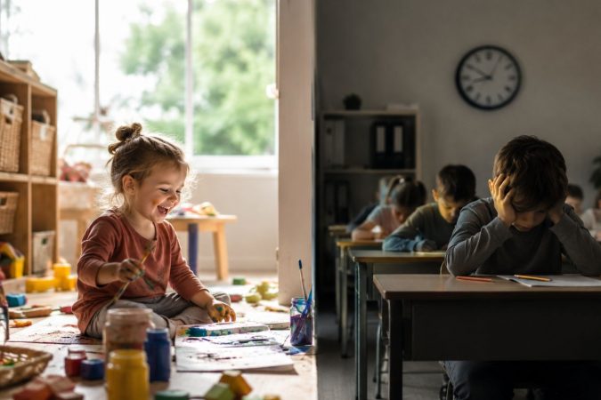 Ein nachdenkliches Kind sitzt allein in einem langen, sterilen Schulflur mit Rucksack und blickt aus einem großen Fenster nach draußen auf eine helle, freie Natur. Der Kontrast zwischen der strengen Schulumgebung und der offenen Außenwelt symbolisiert Leistungsdruck, verlorene Unbeschwertheit und den Wunsch nach freier Entfaltung.