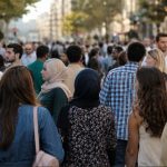 Menschen unterschiedlicher Herkunft bewegen sich auf einer belebten städtischen Straße. Die Aufnahme zeigt eine vielfältige Gruppe von Passanten in einer urbanen Umgebung bei Tageslicht.