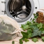 Efeublätter in einem Wäschenetz neben einer Waschmaschine und einem Wäschekorb mit frischer Wäsche.